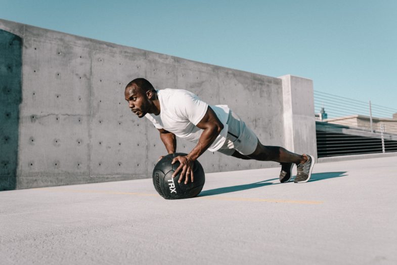 man in white t-shirt and black pants playing with black soccer ball. Medicine Ball Explosive Pushup